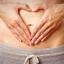 Woman making a heart shape from hands on belly