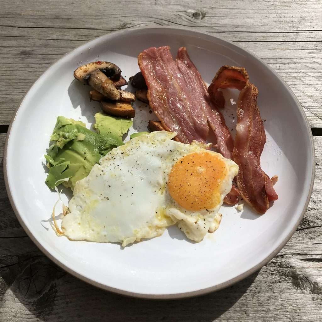 keto, breakfast, english breakfast. A white plate with avocados, eggs, bacon, and mushrooms on it.