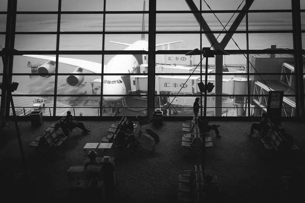 A black and white view looking out from an airport at an airplane pulled up to a terminal.